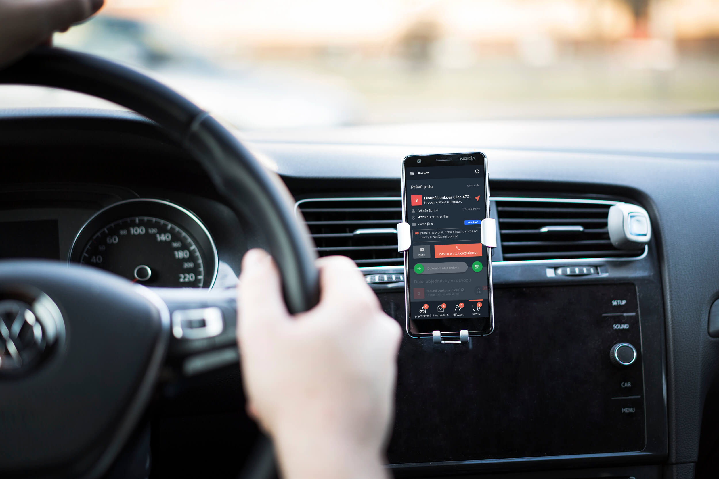 pohled do auta, kde řidič veze objednávku, ve stojánku má mobil s aplikací pro řidiče