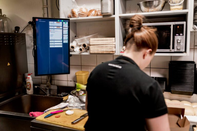 obsluha, která připravuje objednávku v kuchyni, vedle ní je obrazovka pro správu objednávek